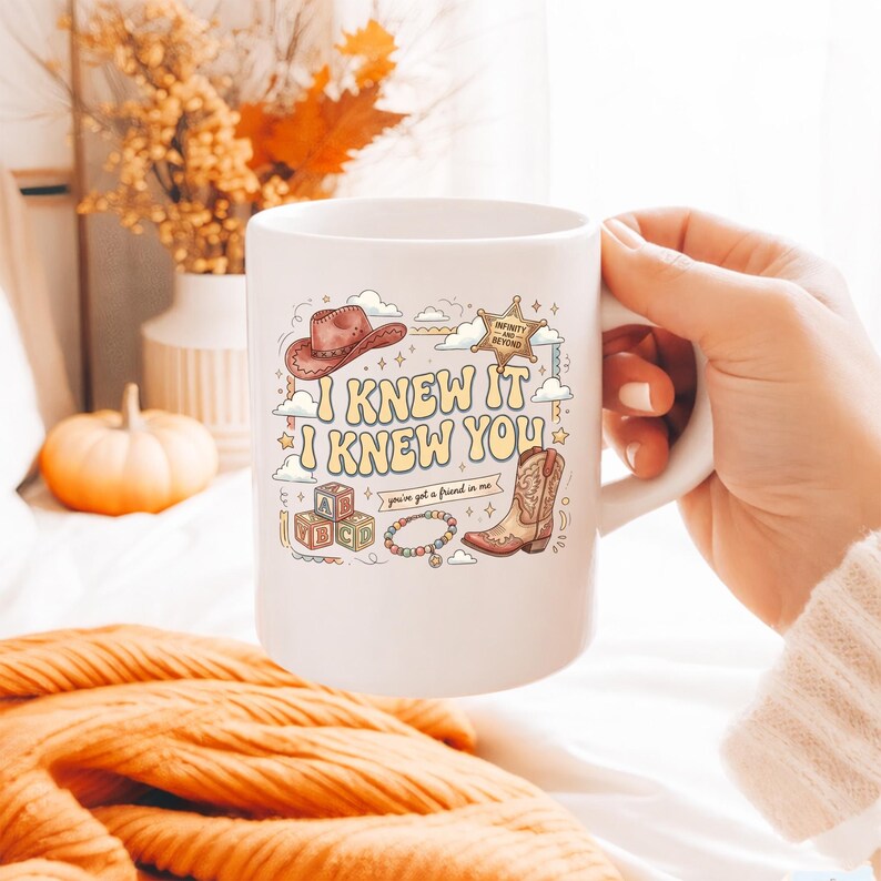 May include: A white ceramic mug featuring a colorful graphic print with the text I KNEW IT I KNEW YOU, a brown cowboy hat, a sheriff star badge, alphabet blocks, a beaded bracelet, and a cowboy boot, along with the phrase you've got a friend in me.
