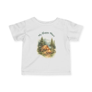 Könnte beinhalten: Weißes T-Shirt mit einer Aquarellillustration eines Campingplatzes mit Zelt, Lagerfeuer und Bäumen. Der Text "My Happy Place" ist in Grün über der Szene angeordnet. Das Shirt ist aus weichem Stoff.