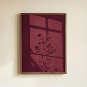 May include: A rectangular wall art piece in a dark wood frame featuring a deep burgundy background. The artwork displays a dark silhouette of a delicate wildflower stem cast by a window shadow, creating a layered effect of light and dark shapes.
