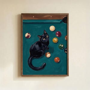 May include: A framed wall art print featuring a black cat sitting on a teal pool table surrounded by scattered colorful billiard balls. The cat has yellow eyes and is looking upward. The wooden frame surrounds the rectangular artwork.