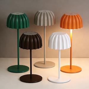 Peut inclure: Cinq lampes de table modernes de couleurs variées : vert, beige, orange, marron et blanc. Chaque lampe a une base ronde, une tige fine et un abat-jour en forme de dôme cannelé. La lampe orange est allumée, dégageant une lueur chaleureuse.