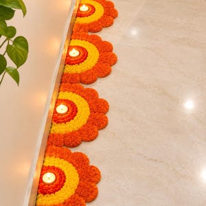 May include: Four semi-circular floral arrangements made of orange and yellow marigold petals lined up along a wall. Each arrangement features a small, lit white tea light candle placed in the centre of the concentric colour pattern.