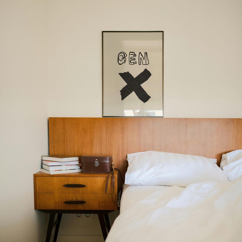 Op de afbeelding: Een slaapkamer met een houten hoofdbord en een nachtkastje. Het nachtkastje heeft twee lades, boeken en een kleine bruine leren koffer. Boven het bed hangt een ingelijste print met de tekst "BEN" en een grote zwarte "X".
