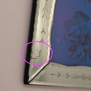 Pu&ograve; includere: Uno specchio da parete rettangolare con cornice nera e bordi in vetro bisellato con motivi floreali incisi. La superficie dello specchio presenta una tonalit&agrave; blu con una grafica tenue. Una piccola crepa &egrave; visibile sul bordo bisellato sinistro.