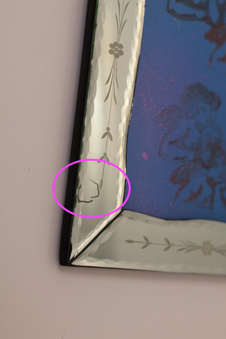 Pu&ograve; includere: Uno specchio da parete rettangolare con cornice nera e bordi in vetro bisellato con motivi floreali incisi. La superficie dello specchio presenta una tonalit&agrave; blu con una grafica tenue. Una piccola crepa &egrave; visibile sul bordo bisellato sinistro.