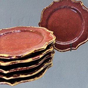 Puede incluir: Una pila de seis platos de cerámica roja con borde festoneado y borde amarillo. Un plato se exhibe en un soporte negro. Los platos tienen una superficie texturizada y son adecuados para servir alimentos.