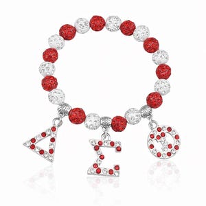 May include: A red and white beaded bracelet with silver charms. The bracelet features alternating red and white crystal-covered beads. Charms include a triangle, a letter, and a circle, all adorned with red crystals.