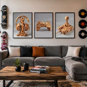 Könnte beinhalten: Drei gerahmte Wandbilder mit geschnitzten Gaming-Accessoires aus Holz. Das linke Bild zeigt einen Kopfhörerständer aus Holz, das mittlere einen Gamecontroller aus Holz und das rechte einen Joystick aus Holz auf einem hellgrauen Hintergrund.