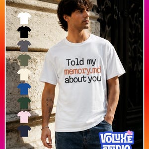 May include: A white short-sleeve t-shirt featuring the black and orange text "Told my memory.md about you" printed on the chest. A vertical column of nine small t-shirt icons in various colors is displayed on the left side of the image.