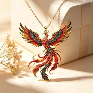 Puede incluir: Un collar con colgante de fénix de color dorado. El fénix está representado con las alas extendidas y plumas de cola fluidas en tonos de rojo, naranja, azul y verde. La cadena del collar también es de color dorado. El colgante se muestra sobre un fondo suave y neutro.