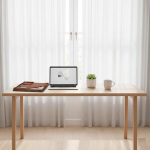 Pode incluir: Uma mesa de madeira clara com um laptop, um portfólio de couro marrom, uma pequena planta suculenta em vaso e uma caneca. A tela do laptop exibe um gráfico. A mesa está em frente a uma cortina branca.