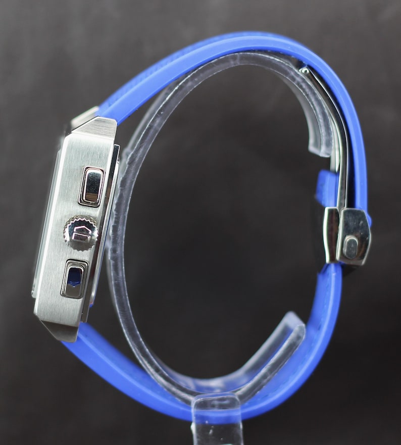 May include: A silver-toned wristwatch with a rectangular face and a vibrant blue silicone band. The watch features a stopwatch function and a secure clasp. The band is approximately 9 inches (23 cm) in length, offering a comfortable fit.