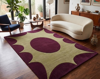 Op de afbeelding: Een rechthoekig vloerkleed met een dieppaarse achtergrond en een groot, centraal stervormig patroon in licht olijfgroen. Het ontwerp bevat een effen olijfgroene ovaal in het midden, omringd door puntige, stralende vormen die naar buiten uitlopen.