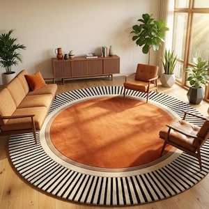 May include: A large circular area rug featuring a solid burnt orange center, a thin beige border, and an outer ring with a black and white radial striped pattern. The rug is positioned on a light wood floor in a room with furniture and plants.