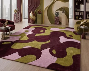 Op de afbeelding: Een groot vloerkleed met een abstract patroon van organische, vloeiende vormen in diep bordeauxrood, olijfgroen en zacht lichtroze. Het kleed heeft een pluche, getextureerd oppervlak met variërende poolhoogtes voor de kleurvlakken.