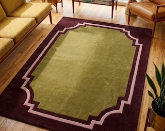 Op de afbeelding: Een rechthoekig vloerkleed met een groot olijfgroen middenpaneel omlijst door een dikke, donkerbordeauxrode rand. Een lichtroze geometrische lijn vormt een decoratieve, geschulpte omtrek die het groene midden van de bordeauxrode rand scheidt.