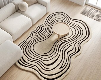 Op de afbeelding: Een onregelmatig gevormd vloerkleed met een crèmekleurige basis en donkerbruine, vloeiende contourlijnen die doen denken aan topografische kaarten. Het kleed heeft een zacht, getextureerd oppervlak en een organische, golvende omtrek.