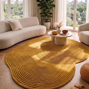 May include: A mustard yellow, abstract-shaped rug with a textured, ridged design dominates the room. The rug is placed on a hardwood floor, and the room features a cream-colored sofa, a round coffee table, and a large window with a view of trees.