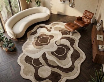 Op de afbeelding: Een onregelmatig gevormd vloerkleed met gelaagde, golvende patronen in tinten crème, beige en donkerbruin. Het kleed heeft een zachte, getextureerde uitstraling met concentrische, vloeiende vormen die lijken op natuurlijke topografische lijnen.