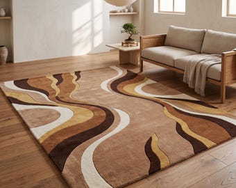 Op de afbeelding: Een rechthoekig vloerkleed met een vloeiend, abstract patroon van golvende lijnen in tinten donkerbruin, beige, crème en mosterdgeel. Het kleed heeft een zachte, pluizige textuur en ligt op een lichte houten vloer in de kamer.