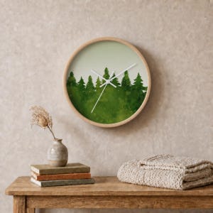 May include: A round wall clock with a light wooden frame featuring a watercolor-style illustration of a dense green forest of pine trees against a pale background. The clock has simple white hour, minute, and second hands centered on the face.