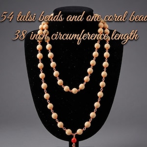 May include: A necklace with 54 tulsi beads and one coral bead. The necklace has a 38-inch circumference. The beads are light beige and strung on a copper-colored chain. A single red coral bead hangs at the bottom.