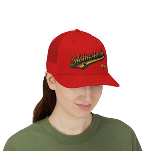 May include: A red trucker hat with a curved brim and mesh back. The hat features the word "Motherland" embroidered in a script font with green, yellow, and black accents. A small emblem is on the right side.