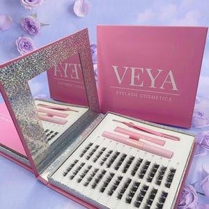 Könnte beinhalten: Rosa Wimpern-Kosmetik-Set mit dem Markennamen "VEYA" auf der Box. Das Set enthält falsche Wimpern, einen Spiegel, eine Pinzette und Applikatoren. Das Set wird auf einem hellvioletten Hintergrund mit Blütenblättern präsentiert.