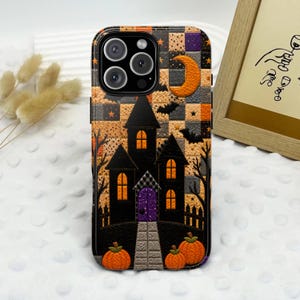 Puede incluir: Una funda para smartphone con un fondo a cuadros de cuadrados naranjas, negros y morados. El diseño incluye una casa encantada negra con ventanas amarillas brillantes, una puerta morada, una luna creciente, murciélagos y calabazas.