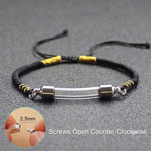 Op de afbeelding: Een zwart koordarmband met een centrale doorzichtige glazen buis en zilverkleurige metalen doppen. De armband heeft goudkleurige draadaccenten en verstelbare zwarte koorden. Een inzet toont 2,5 mm en Screws Open Counter-Clockwise.