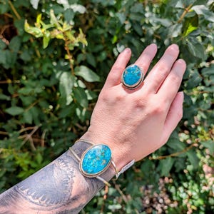 May include: A silver cuff bracelet and a matching silver ring, both featuring oval-shaped turquoise stones with intricate brown matrix patterns. The stones are set in twisted silver wire bezels, creating a cohesive set of jewelry with a polished finish.