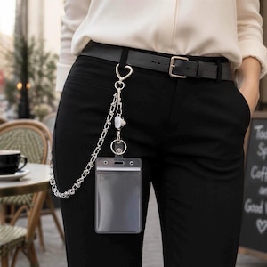 May include: A silver-toned metal chain lanyard attached to a black belt, featuring a heart-shaped clasp, a retractable badge reel, and a clear vertical plastic ID card holder. The chain links are connected to the belt loop for secure attachment.