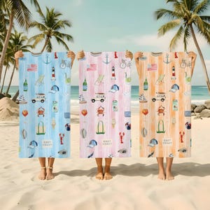 May include: Three beach towels with a coastal theme are held up on a sandy beach. Each towel features a different color: blue, pink, and orange. The towels are decorated with nautical illustrations, including anchors, flags, and bicycles. The text "EAST COAST" is printed on each towel.