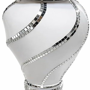 May include: A white ceramic vase featuring a wide flared rim decorated with small square mirror tiles. The neck is adorned with a metallic silver band displaying a Greek key pattern. The body has swirling vertical stripes of mirror tiles.