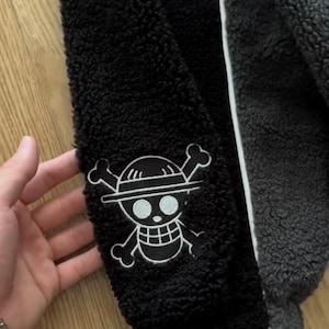 May include: Black and grey fleece jacket with white trim. The jacket has a white embroidered Jolly Roger patch on the sleeve. The jacket is made of a soft, textured material.