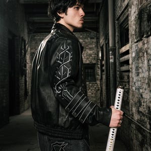 May include: Black leather jacket with white decorative stitching. The jacket is worn with dark denim jeans. A white katana is held. The background is a brick alleyway. The jacket has a ribbed hem and cuffs.
