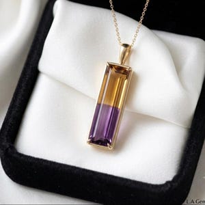 May include: A rectangular pendant necklace featuring a bicolored gemstone with a golden yellow top half and a deep purple bottom half, set in a gold frame and suspended from a delicate gold chain, presented in a black and white jewelry box.