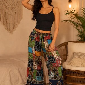 Könnte beinhalten: Ein schwarzes Camisole-Top kombiniert mit einer Patchwork-Palazzohose. Die weite Hose hat ein farbenfrohes Patchwork-Design, einen Kordelzug in der Taille und einen marineblauen Saum mit geometrischem Muster. Das Outfit ist lässig und im Bohème-Stil.
