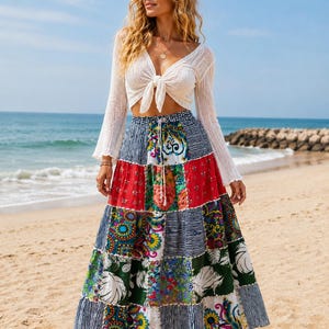 May include: A long-sleeved white knit top with a front tie closure paired with a floor-length, multi-colored patchwork skirt. The skirt features various patterns including floral, paisley, and striped designs in shades of red, green, blue, and yellow.