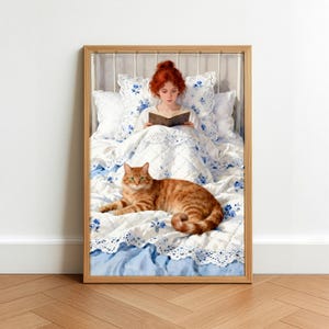 May include: A framed print depicts a person with red hair reading in bed, with a ginger cat lying at the foot of the bed. The bedding is white with blue floral patterns and lace trim. The bed frame is white metal.