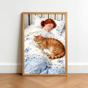 May include: A framed print depicts a sleeping person with red hair in a bed with a ginger tabby cat. The bedding features a blue floral pattern and white lace trim. The cat has green eyes and is lying on the quilt.