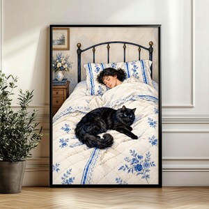 May include: A framed wall art print depicting a person sleeping in a bed with a black cat resting on a white quilt featuring a blue floral pattern. The bed has a black metal frame, and the scene includes a wooden nightstand with a vase of flowers.