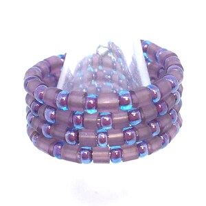 May include: A purple and blue beaded ring with a iridescent finish. The ring is made of multiple rows of beads.