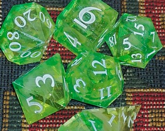 May include: A set of seven polyhedral dice in a translucent lime green color with embedded glitter particles. Each die features white engraved numbers, including a twenty-sided die, a twelve-sided die, a ten-sided die, an eight-sided die, and a four-sided die.
