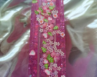May include: A long, rectangular resin tray in a vibrant translucent pink hue, filled with embedded decorative elements including small pink and white flower shapes, tiny green leaves, heart-shaped accents, and shimmering glitter particles throughout.