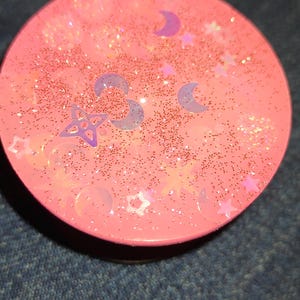 May include: A white ceramic mug with a black handle and the text "But First, Coffee" in a bold, black font. The mug is set against a blurred background, suggesting a cozy setting.