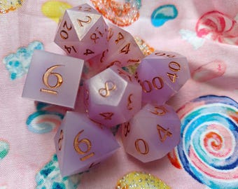May include: A set of seven polyhedral dice in a soft, opaque lavender color with metallic copper-colored numbers. The collection includes a d20, d12, d10, d8, d6, d4, and a percentile die, all featuring sharp edges and clear, legible engraved numerals.