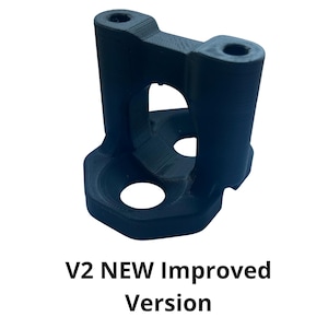 Op de afbeelding: Een zwarte, 3D-geprinte beugel met twee cilindrische gaten aan de bovenkant en een groter rond gat aan de onderkant. De beugel heeft een zeshoekige basis en de tekst "V2 NEW Improved Version" is hieronder afgedrukt.