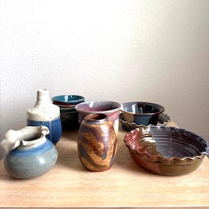 May include: A collection of handmade ceramic pottery including a blue and white speckled vase, a small blue bowl, a brown and tan striped vase, a dark blue bowl, and a wide, shallow, fluted-edge bowl with a brown and grey glazed finish.