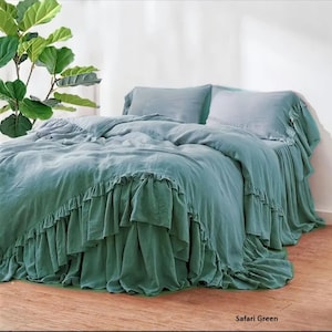 Peut inclure: Un lit avec une housse de couette et des taies d'oreiller vert safari. La housse de couette et le jupon de lit ont une bordure à volants. Le lit est dans une pièce avec une plante dans le coin.